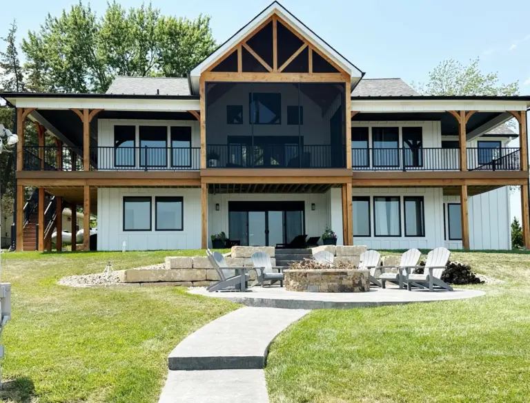 Timber-framed lake house with a screened upper porch and a fire pit patio on the lawn below