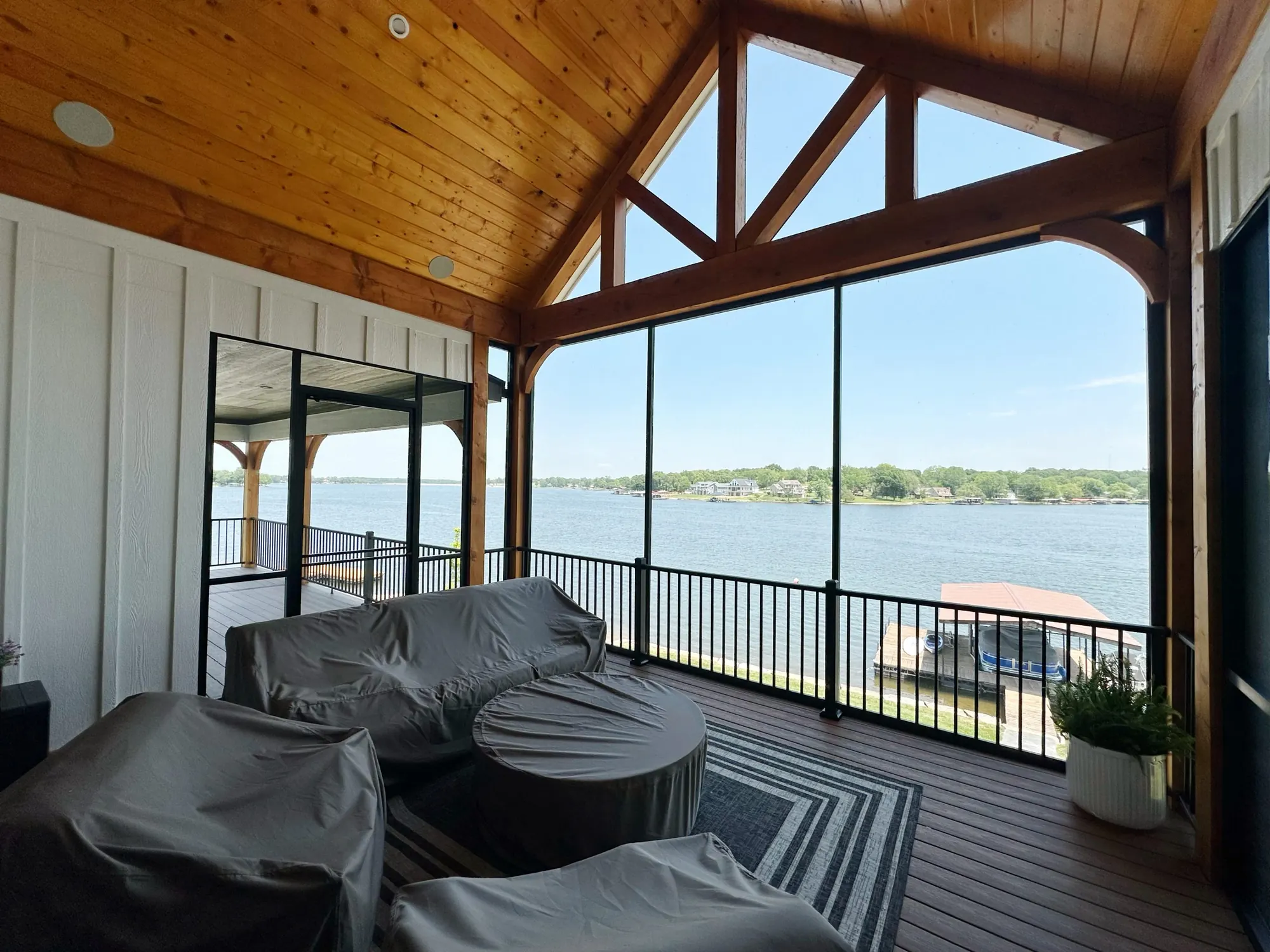 Screened lake porch with a gabled timber ceiling and a wide view of the water and boat docks