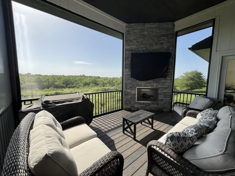 Furnished screened porch with a stone fireplace, wall-mounted TV and wicker seating overlooking open land
